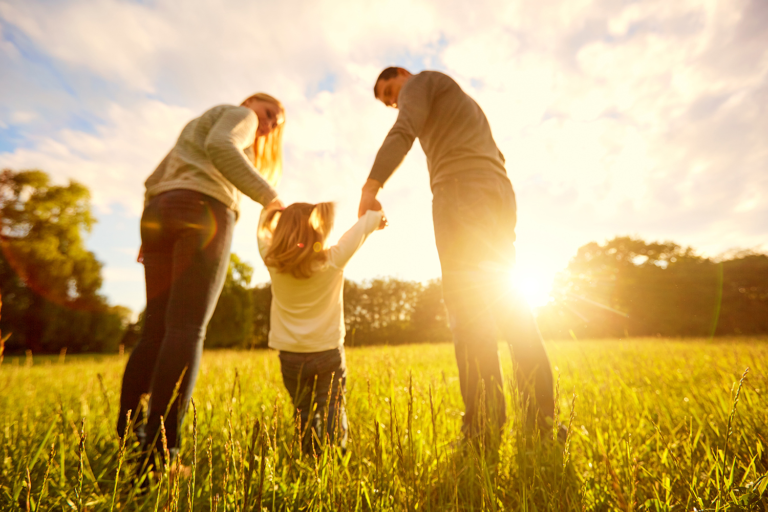 Family with young child walking in field with sunset