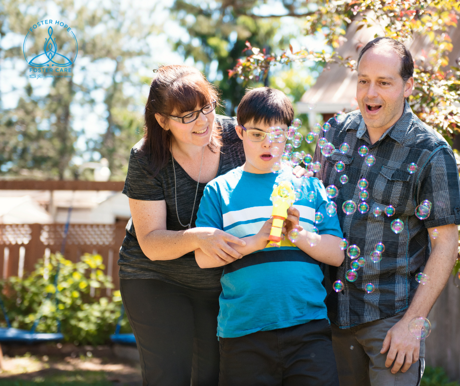 A middle aged woman and middle aged man stand beside a boy of approximately 10 years old.  He holds a bubble machine and looks surprised.