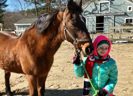 girl with hood standing by horse